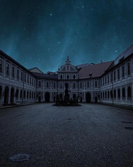 A quiet palace courtyard at night with a central fountain, surrounded by arched buildings under a clear, starry sky.
