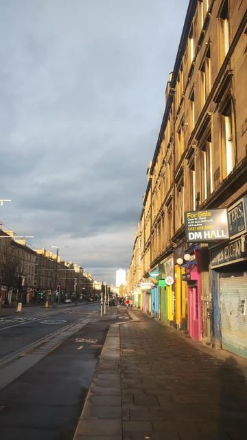 Looking along the wide boulevard of Leith Walk, buildings on the left, the road & pavement all in shadow, an angle of sunlight hitting only the facade of buildings on the right