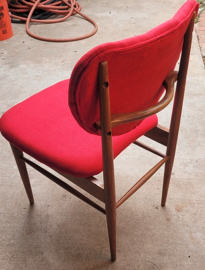 Back side of a red chair with new padding. You can see a hose in the background in a yard.