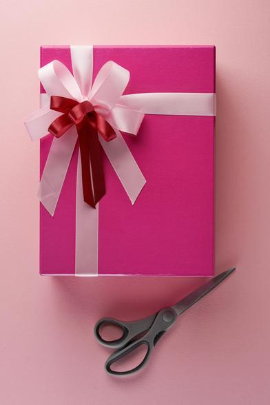 pink gift wrapped with red and with bows, atop a peachy pink table. on the right is a scissor. reminder that presence is a gift, and some gifts are soft and beautifully pink