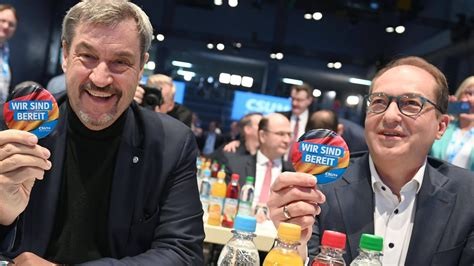 Söder und dobrinth in versammlungssaal an tisch sitzend, zeigen bierdeckel wo draufsteht 'wir sind bereit'.