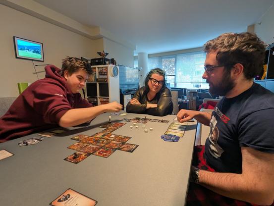 Three people seated around a table playing a tabletop game