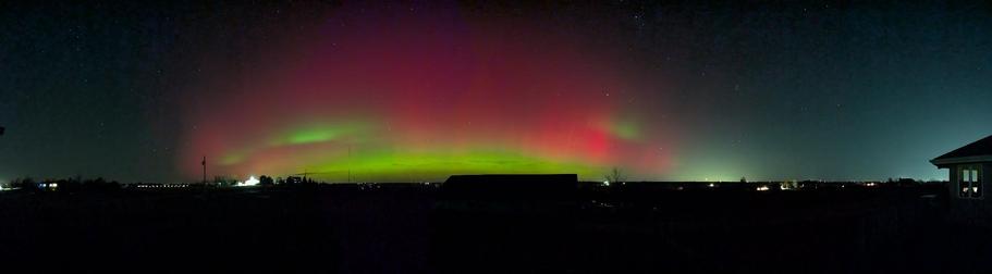 A panorama of a sky filled with red and green aurora