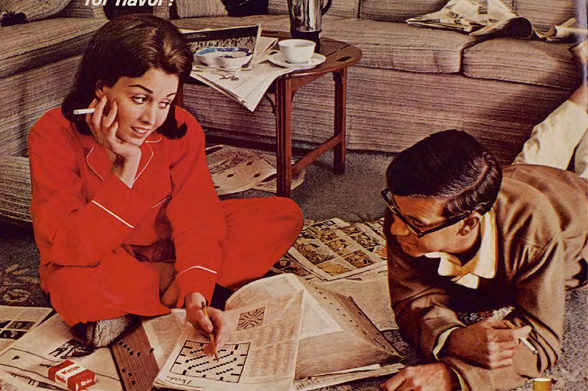 1966 Nostalgic Scene of Two Adults Engaged in Leisure Activities at Home
The image depicts a moment frozen in time, likely from the 1960s or early '70s, capturing two adults engrossed in their respective pastimes.
A woman is seated on the floor with her legs spread out before her, dressed in bright red pajamas and smoking what appears to be a cigarette.
She's deeply focused on solving a crossword puzzle featured prominently in front of her.