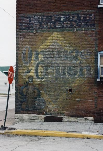 A faded advertising sign for Orange Crush soda, painted on the exterior wall of a red brick building.