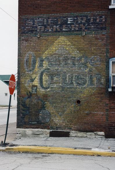 A faded advertising sign for Orange Crush soda, painted on the exterior wall of a red brick building.
