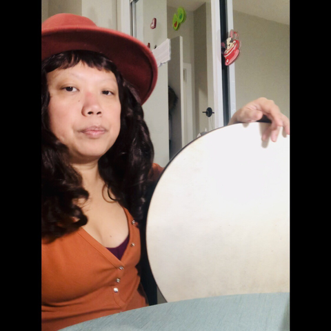 Me wearing orange hat and top, holding a Turkish bendir drum 18” goatskin head