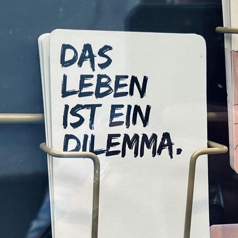 Eine Karte in einem Schaufenster wo draufsteht „Das Leben ist ein Dilemma“.