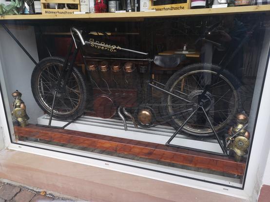 In einer Schaubox im unteren Teil eines Schaufenster ist das Nachbaumodell eines frühen englischen Motorrads (Brough Superior) ausgestellt