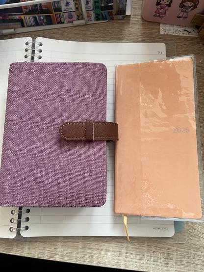 A6 daily undated notebook in a purple cloth cover next to 2026 weekly notebook with an orange paper cover and plastic sleeve
