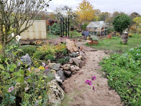 Pflaster und Beetumrandungen raus, Beet erweitern und Trockenmauer aus vorhandenen Rheinkieseln aus dem entfernten Teich bauen