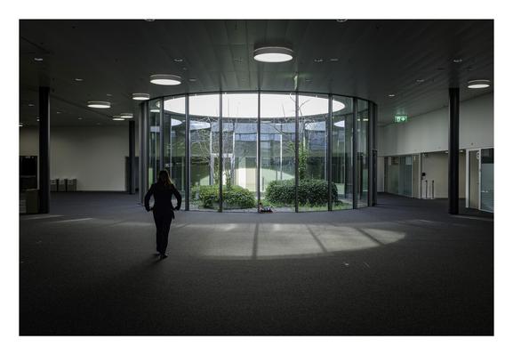 Une personne, de dos, dans les sous-sols du SwissTech Convention Center. Au second plan, un puits de lumière vitré, dans lequel se trouvent des arbres