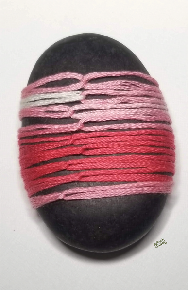 Photo of a black oval stone wrapped in variegated pink embroidery thread using a paracord wrap style.