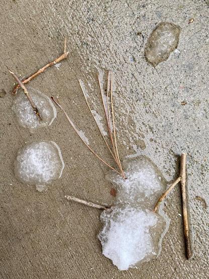 Color image of the two snowmen melted away on the porch, their snow body balls now shaped as circles on the porch floor. Image shows four snowy melted circles of what were snowmen bodies, and their twig arms detached.