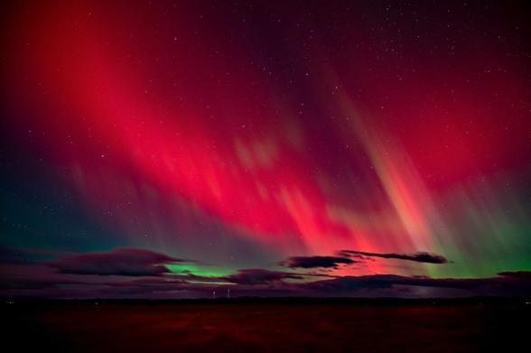 Vivid red and green northern lights illuminating the night sky above a dark, cloud-covered landscape.