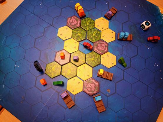 Blick von oben auf das Spielfeld. In der Mitte die Insel, darum herum Flöße, Monster und verzweifelte Meeples.