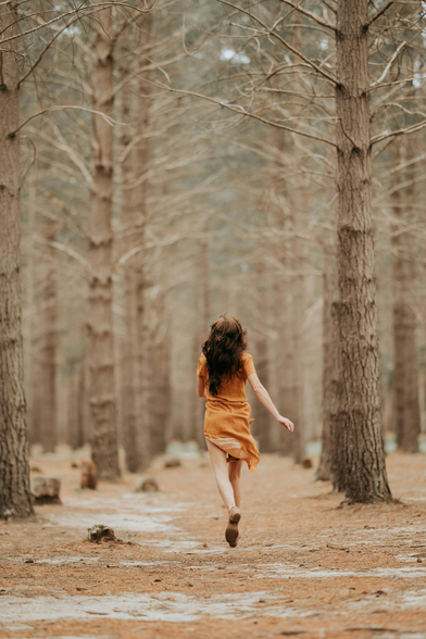 Red haired woman in orange dress running into a bare autumn forest