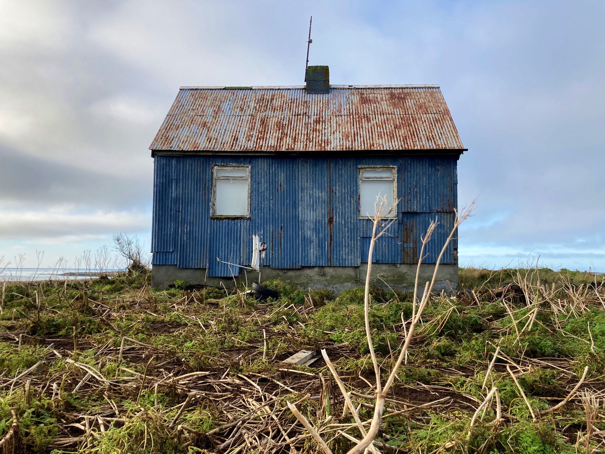 An abandoned blue house with a rusty roof.