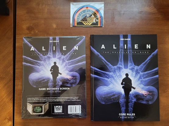ALIEN RPG, Game Mother's Screen, and USCSS Fidanza patch. Covers of book and GM screen feature a human silhouette armed with a flame thrower in foreground. The background is a giant facehugger X-ray.