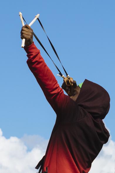 La photographie d'un jeune homme encapuchonné tendant vers le ciel un lance pierre (dans lequel il y a une boule de graines)