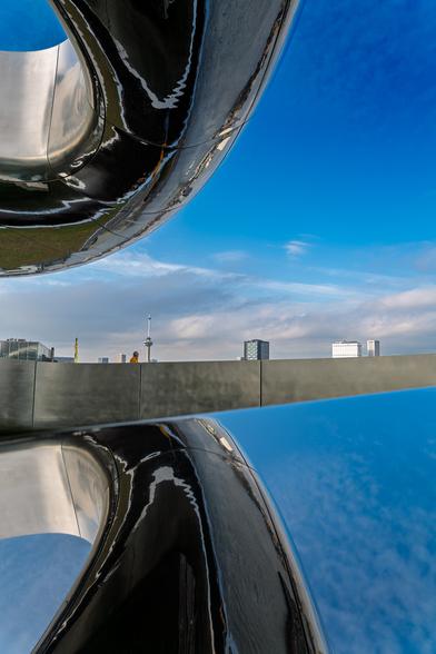 Onder en boven is een zilveren en glanzende boog te zien. De foto lijkt in tweeën gesplitst. Onder en boven is namelijk lucht te zien doordat een glad oppervlak onder de lucht spiegelt.