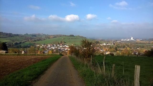 Panorama sur Lamorteau depuis les hauteurs. Un chemin au milieu de l'image et un paysage de cuestas verdoyantes, à droite dans le fond, la Cellulose des Ardennes, seule industrie de la région encore en activité.