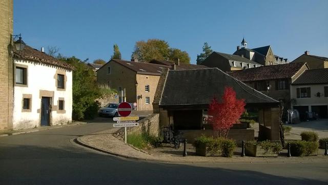Le Lavoir de Torgny dans le centre du village sur une petite place entourée de maisons diverses, dans le fond, sur les hauteurs, on peut voir l'église du village.