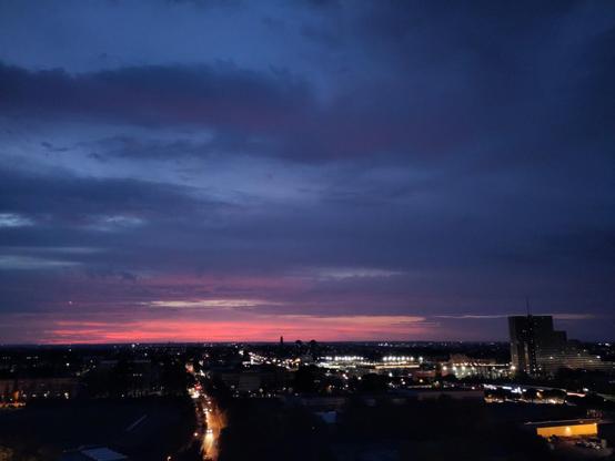 aube naissante avec les nuages bleu et le fond du ciel rose, la ville en bas piqueté de lumières telles des étoiles
