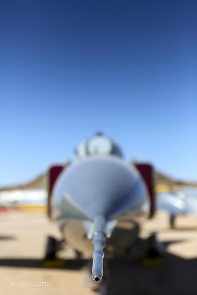 This is an abstract colour photo of the nose of a cold war Soviet MiG-23 fighter jet. Tucson, Arizona (2013).

At the base and in the centre of the image is a narrow, hollow, shiny, metal tube that extends back about a quarter of a metre and gradually blurs out of focus. Beyond is a large, round, nose cone. Behind and blurring further are two rectangular, in the vertical plane, air-intakes both with red blanks inserted. Above is the semi-circle of the canopy with a egg shaped metal frame facing forward. The inboard section of the wings are so blurred it's more left to the imagination. Below the jet is a yellow sandy surface, above, is a clear and cloudless blue sky, graduating darker towards the top of the photo.
