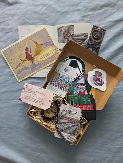 Colis ouvert comprenant des stickers, carte et un magnifique porte clé et un bracelet tout aussi beau. Du noir du rouge et trois flèches dans un cercle...