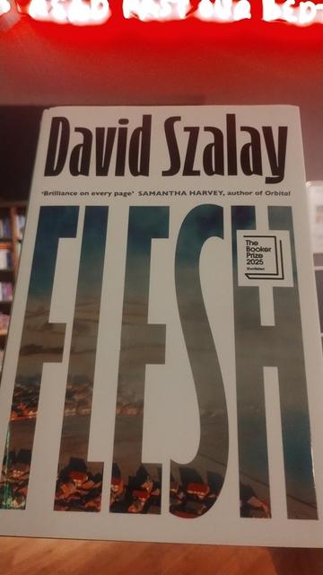 Hardback copy of David Szalay's Booker Prize winning novel, Flesh, a white cover with "FLESH" in tall, thin letters across the front