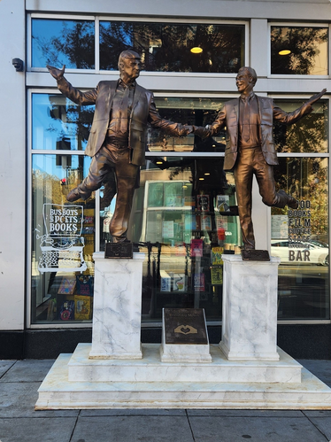 A bronze statue of Trump and Epstein holding hands and frolicking together on a marble base. There's a deliberately annoying inscription with a pair of hands in a heart also on the base. The statue is outside the windows of a DC bookstore.