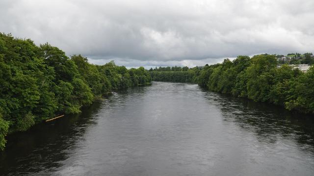 A photo of a river with trees lining both sides. The sky is filled with clouds.
