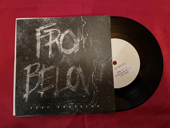 An image of a vinyl record test pressing with a black cover, featuring the text "FROM BELOW" in a graffiti-like style. The record is partially visible, showing a white label with text indicating it is a test pressing.