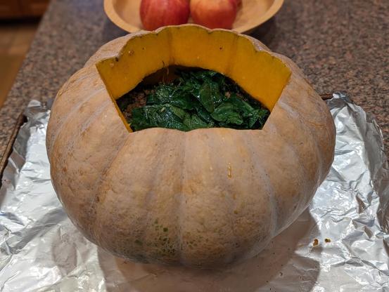 enormous uncooked pumpkin stuffed with lamb, kale, & bulgur wheat on a tinfoil-lined half sheet pan