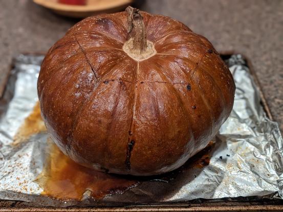 gorgeous brown cooked pumpkin with it's hat on, leaking delicious juices all over the tinfoil