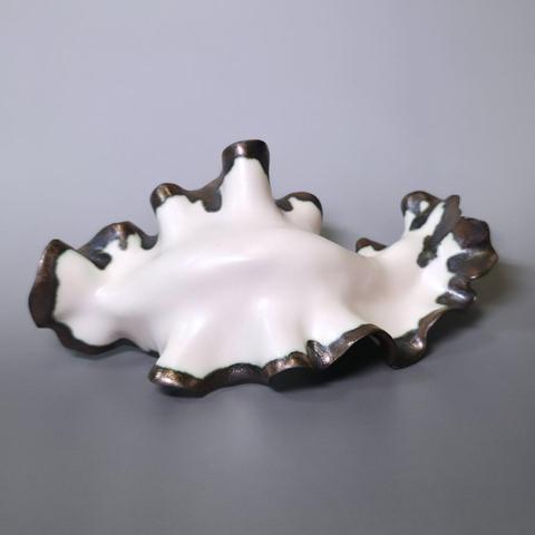 Abstract handmade ceramic sculpture made out of white stoneware clay with golden glazed edges depicting a nudibranch/seaslug on a grey background