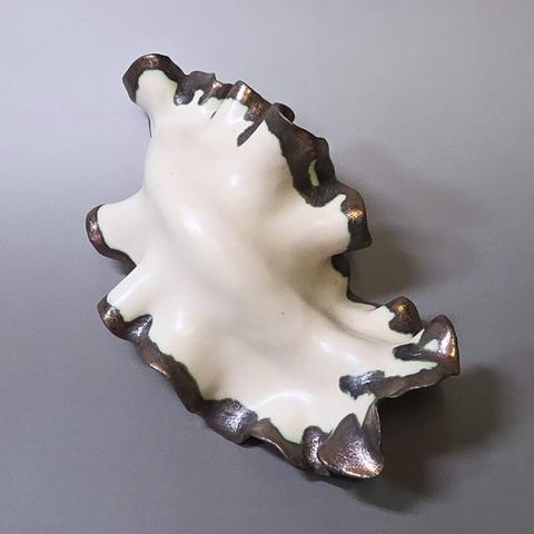 Abstract handmade ceramic sculpture made out of white stoneware clay with golden glazed edges depicting a nudibranch/seaslug on a grey background
