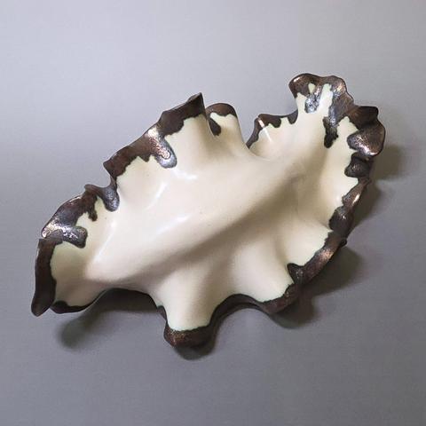 Abstract handmade ceramic sculpture made out of white stoneware clay with golden glazed edges depicting a nudibranch/seaslug on a grey background