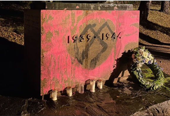 Kuvakaappaus Hesarin jutun kuvan osasta. Muistomerkin paasi, jota spreijattu pinkillä maalilla, keskellä, vuosilukujen 1939 - 1944 päälle on maalattu mustalla kuvio, joka ei ole hakaristi, mutta sellaiseksi ilmeisimmin tarkoitettu.
Paaden edessä on hautakynttilöitä ja seppele.