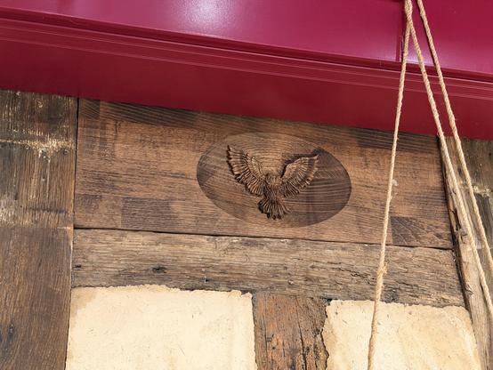 CNC carving of a stylized owl with wings outstretched in a block of wood installed in a gap between timbers