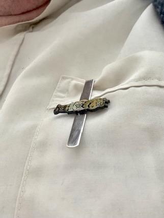 Eine Krawattenklammer mit TeX-Löwe, um 90° an eine Hemdentasche geklemmt, sodass sie wie ein Kreuz aussieht (mit Löwe als Querbalken).