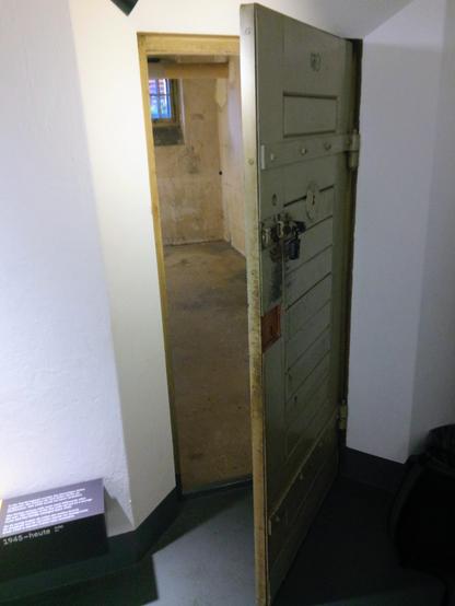 Die einzige erhaltene Zellentür, grün-grau, erlaubt leicht geöffnet den Blick in den Haft ehemaligen Haftraum dahinter.
