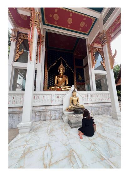 Fotografía de una mujer sentada en el suelo frente a una figura de Buda en el templo Wat Saket Ratchawora Mahawihan.