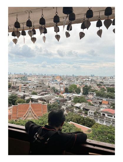 Fotografía de un hombre joven de espalda, el hombre está recostado a una ventana viendo la ciudad de Bangkok desde el templo Wat Saket Ratchawora Mahawihan.