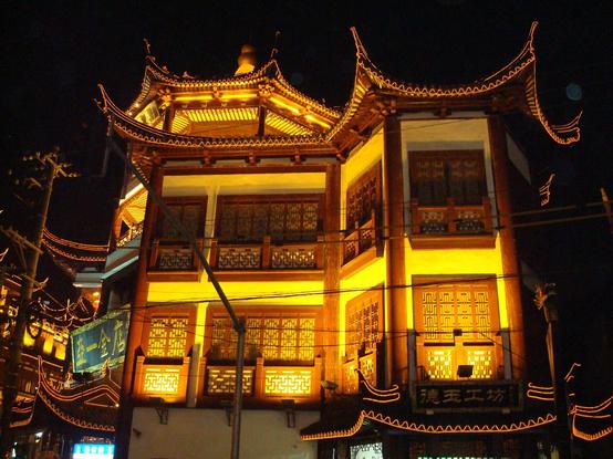 Bâtiment moderne de style traditionnel chinois, fenêtres aux cadres de bois rouge et toits pointus, éclairé de nuit, à Shanghai.