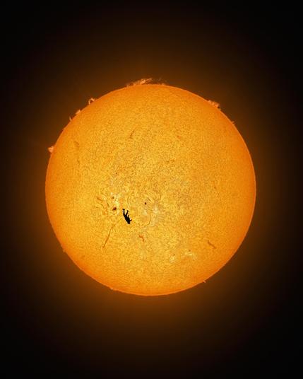 A wider view of a human in free fall in front of the sun. The full disk of the sun is in the frame surrounded by blackness. The human figure is at the bottom left, head down. The human's size compared to the sun is miniscule.