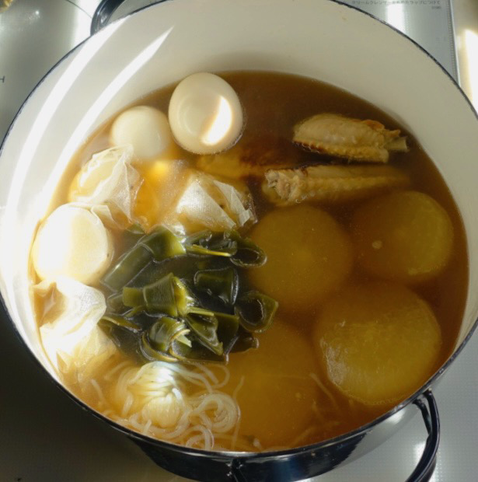 琺瑯鍋で煮込まれている鶏手羽中、大根、結び昆布、白滝、たまご、お茶パックに入った長芋が写っている。