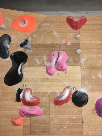 Climbing wall with a problem set with red and pink holds. In the middle of wall are two big pink holds facing each other, the space between them forming a vertical crack.