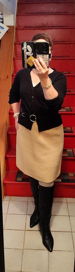 Black cardigan, belted, over slightly short beige-y yellow wool skirt. Beige tights, black knee high pointy boots. Pearl and white jewelry.